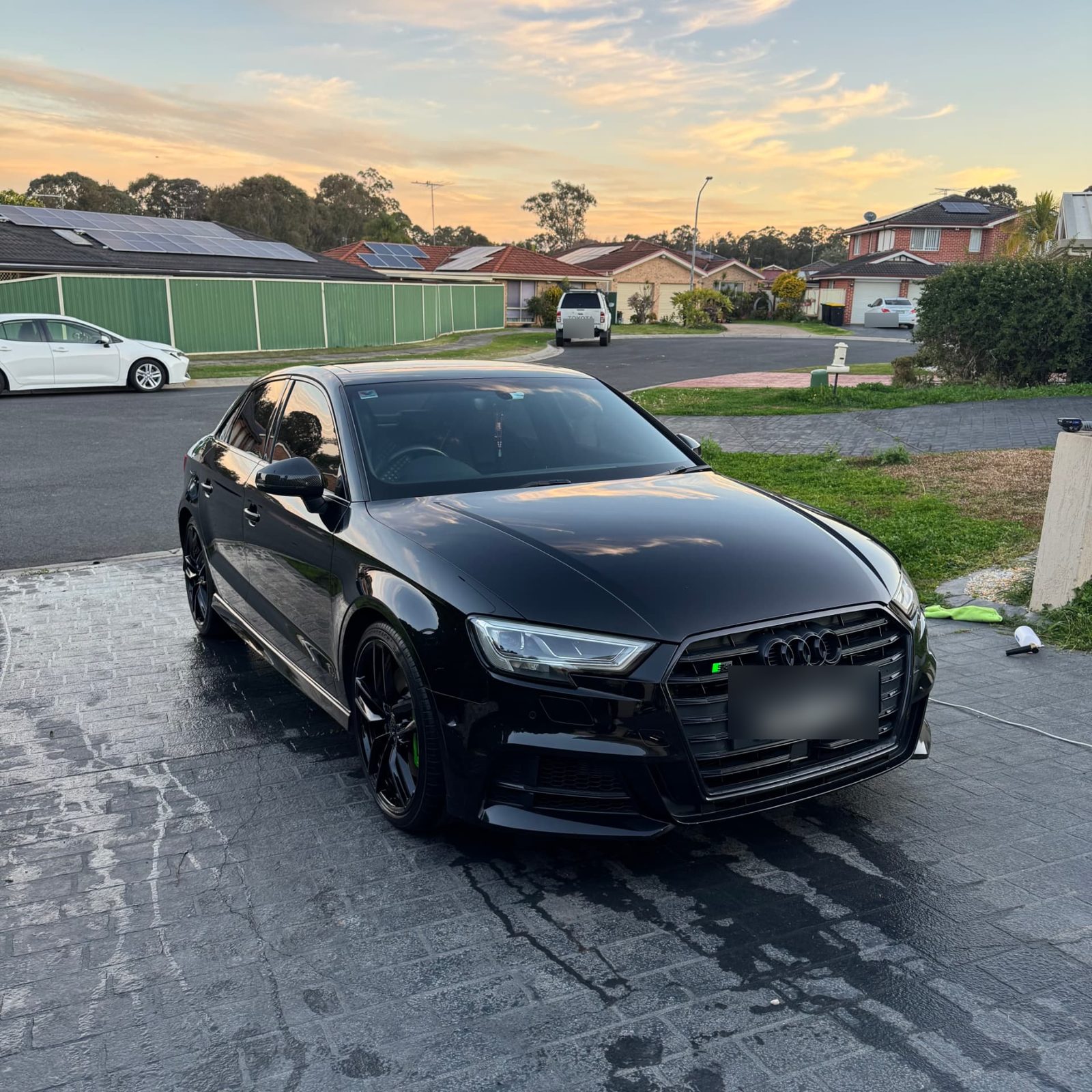 Black Audi S3 sedan freshly detailed on a wet driveway at sunset