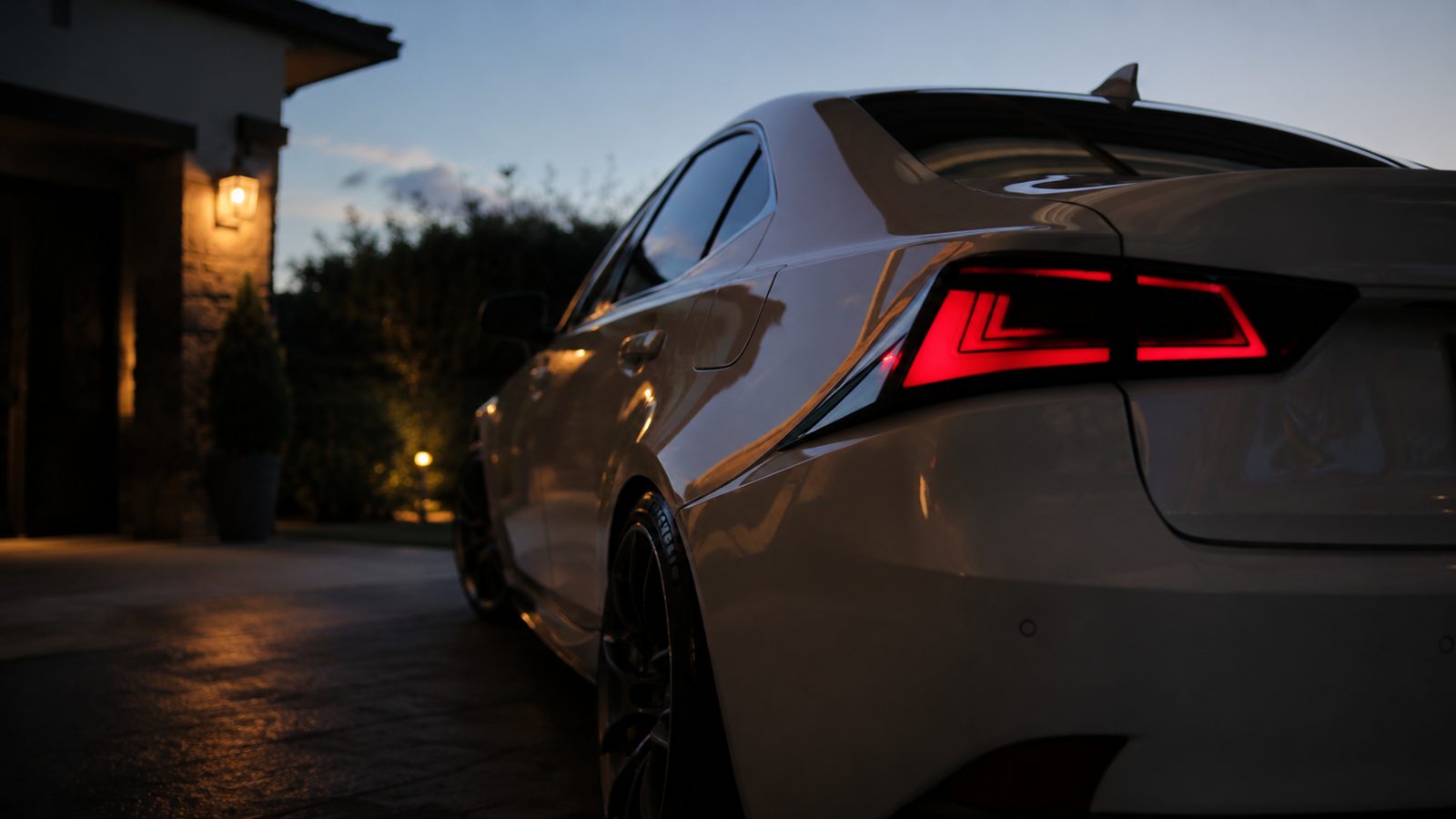 White Lexus IS rear quarter glowing under porch lights at dusk