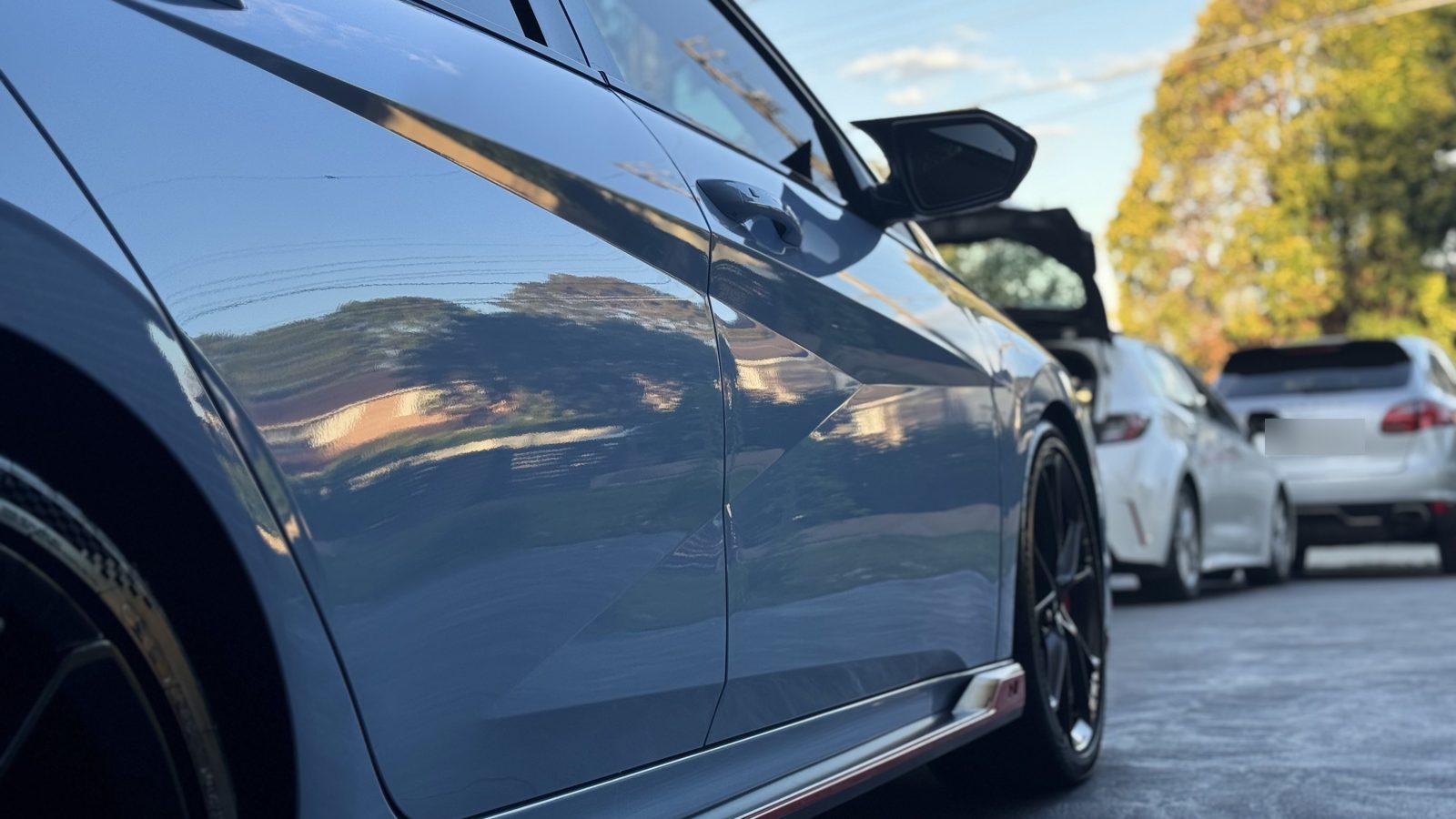 Glossy ceramic-coated blue door panels of a Hyundai i30 N reflecting houses and sky