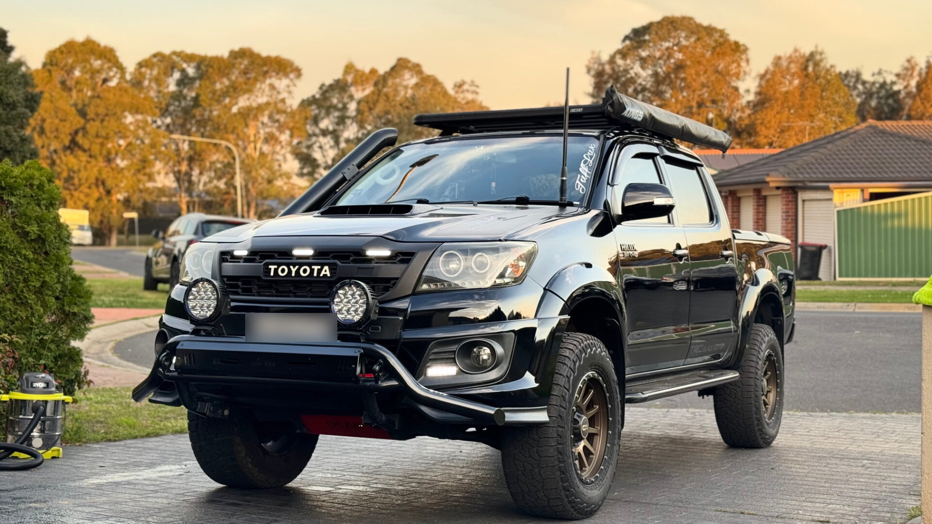Black Toyota Hilux after paint correction and ceramic coating, front three-quarter view at sunset